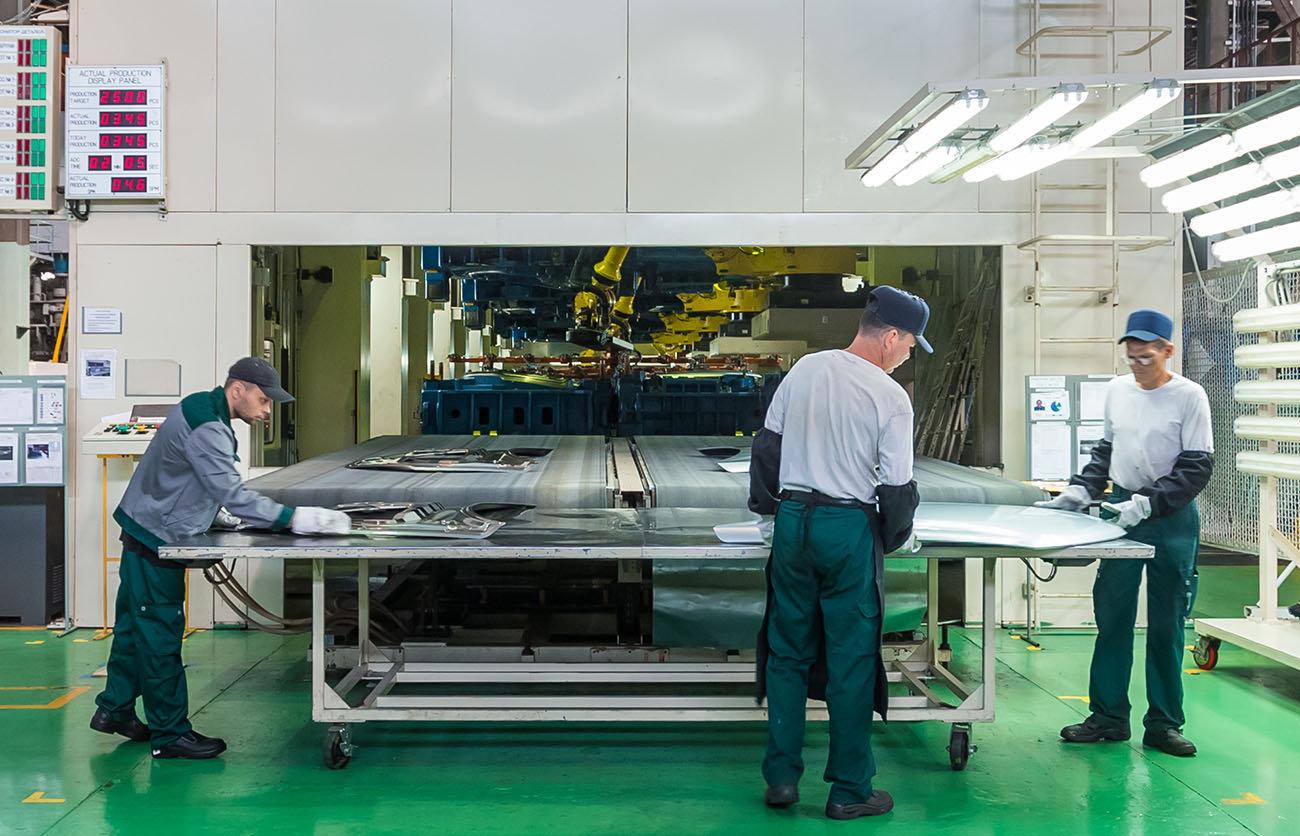 3 people working in factory at conveyor belt exit of a large machine